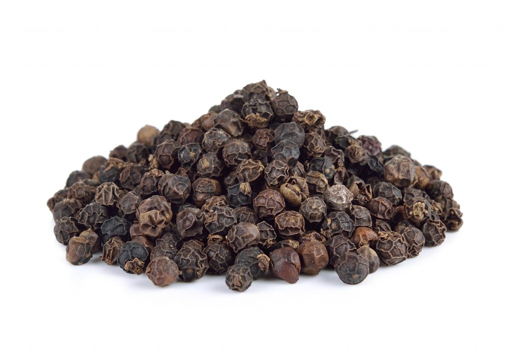 whole black peppercorns on white background