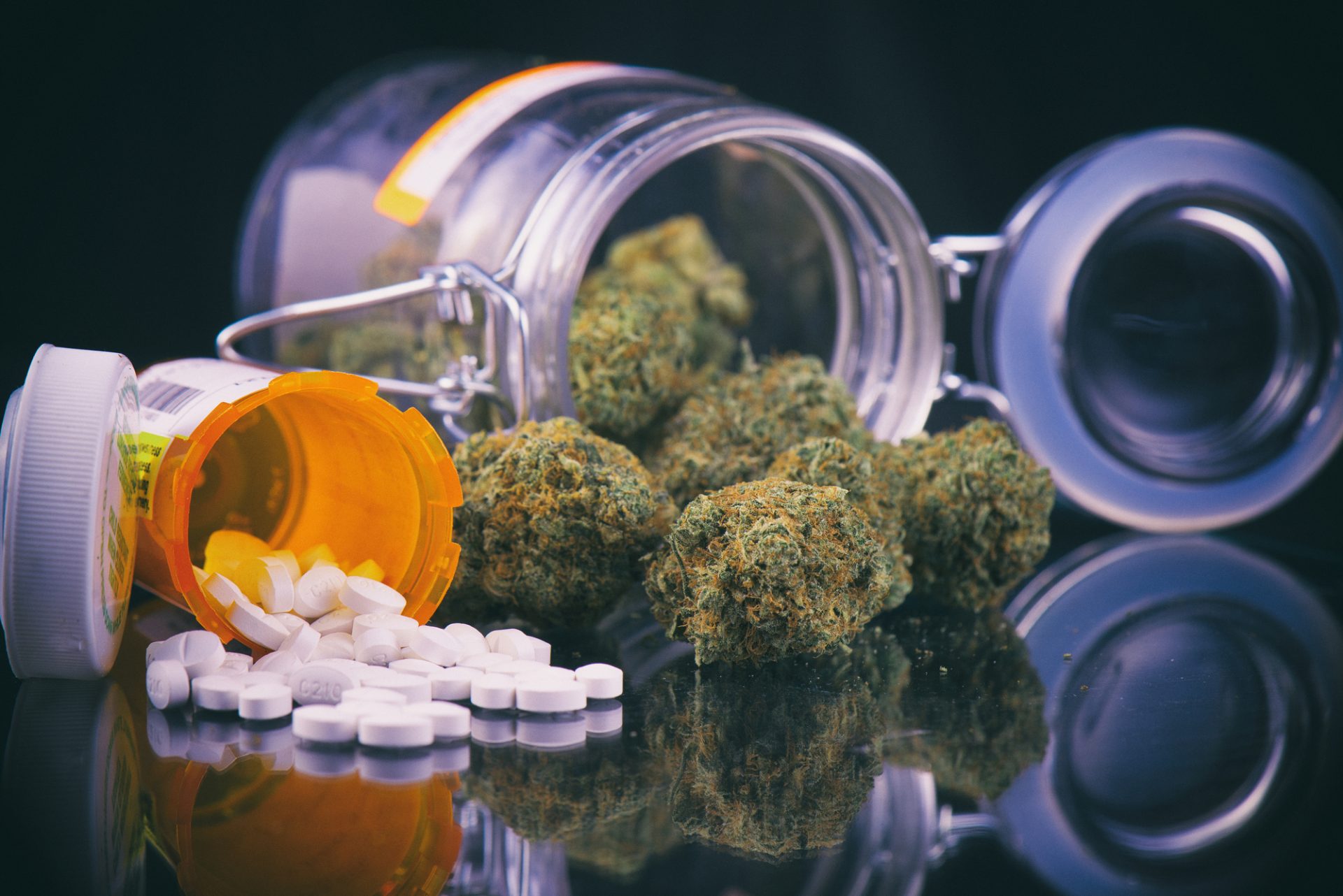 cannabis and drug interactions: Detail of cannabis buds and opioid pills over reflective surface - medical marijuana dispensary concept