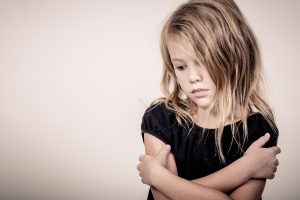 autism and cannabis: Portrait of sad blond little girl standing near wall
