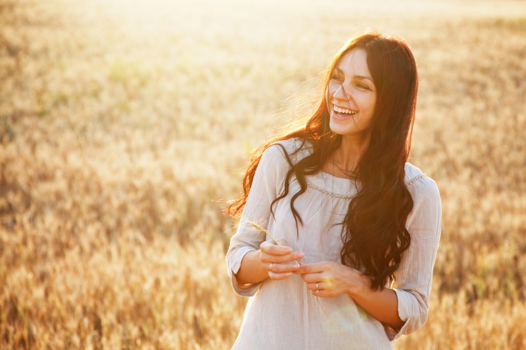 Smiling brunette lady in wheat field at sunset
